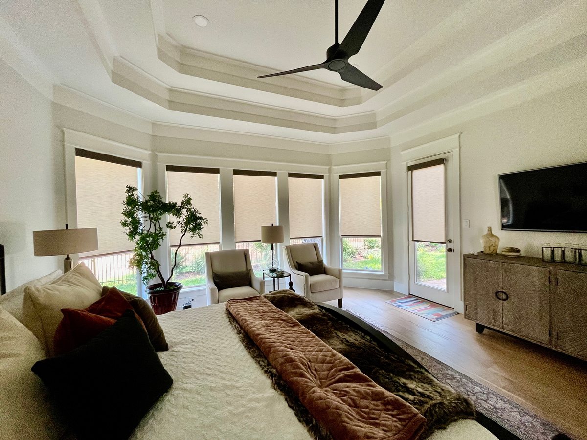 Master bedroom with a bay of custom roller shades by Love Is Blinds